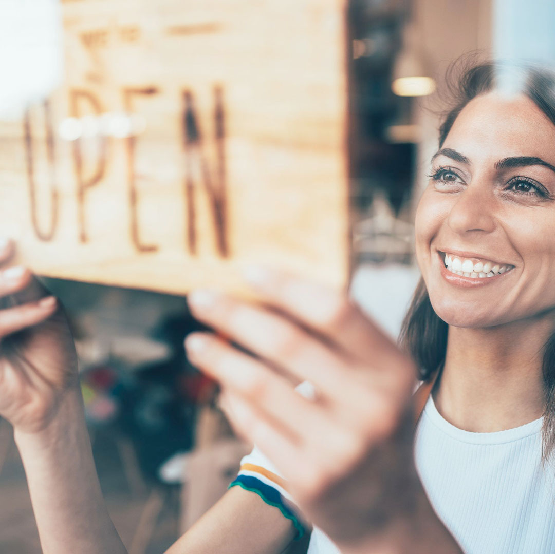 A woman displaying an open sign on a shop door