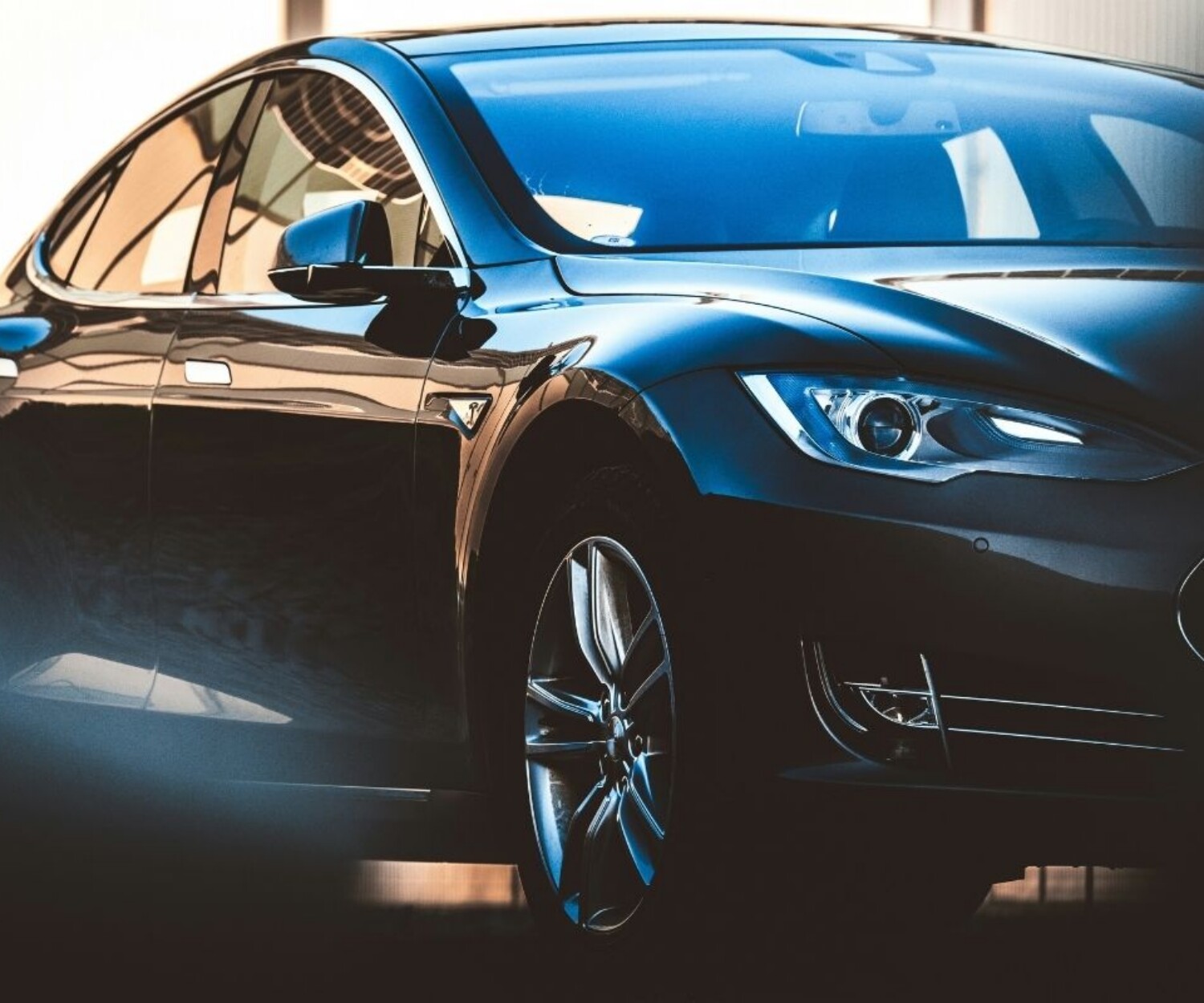 Black luxury sedan photographed from a low front-left angle, showing glossy curves and chrome wheel in a showroom lighting.