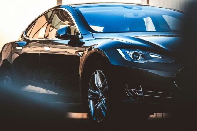 Black luxury sedan photographed from a low front-left angle, showing glossy curves and chrome wheel in a showroom lighting.