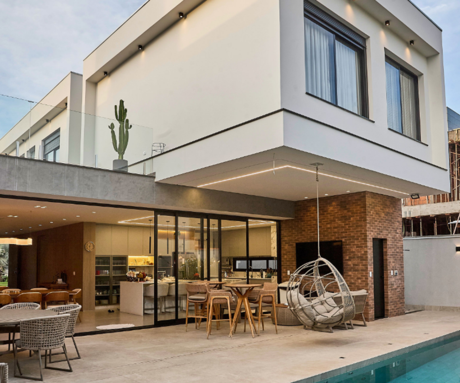 Modern two-story home with a glass-wrapped terrace, outdoor seating, a hanging egg chair, and a pool.
