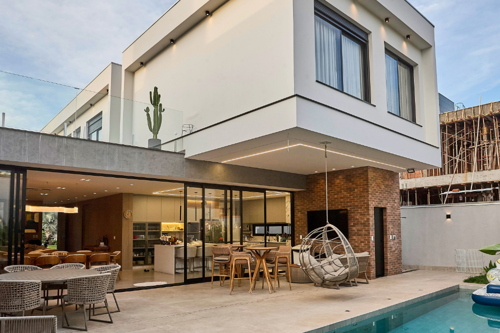 Modern two-story home with a glass-wrapped terrace, outdoor seating, a hanging egg chair, and a pool.