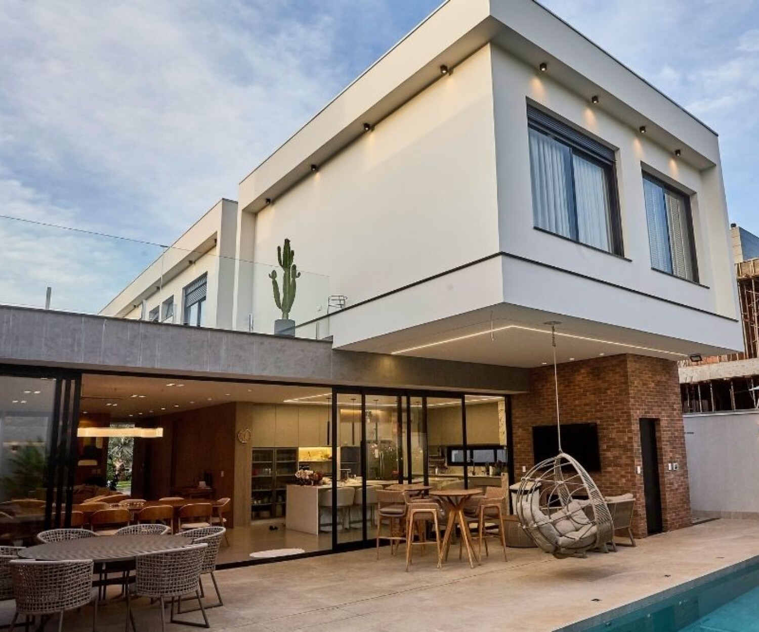 Modern two-story home with a glass-wrapped terrace, outdoor seating, a hanging egg chair, and a pool.