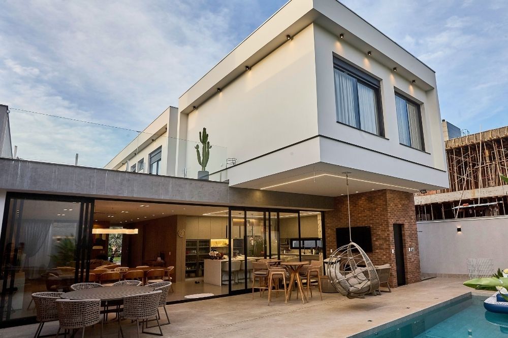 Modern two-story home with a glass-wrapped terrace, outdoor seating, a hanging egg chair, and a pool.