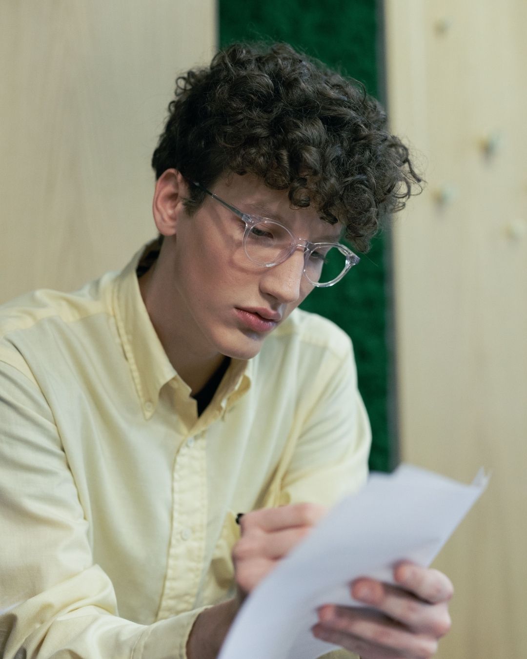 Man in yellow button-up shirt looks serious while doing paperwork.