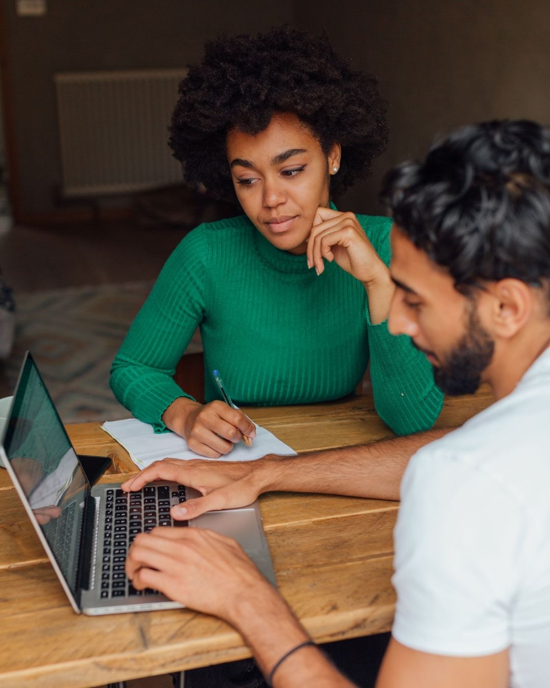 Woman in green sweater and a man look at a laptop screen.