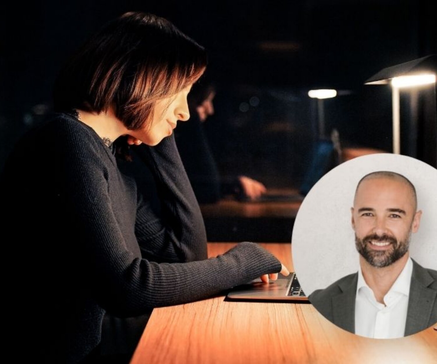 Woman typing on a laptop at a wooden desk in dim light; a circular portrait of a smiling man in a suit sits nearby.