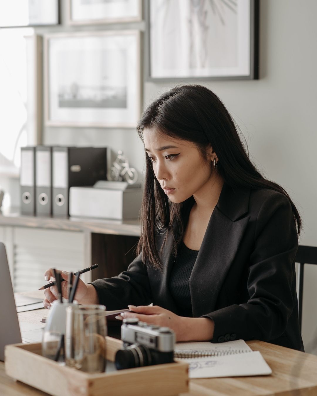Lady in black blazer sits at her desk and does work on her laptop.