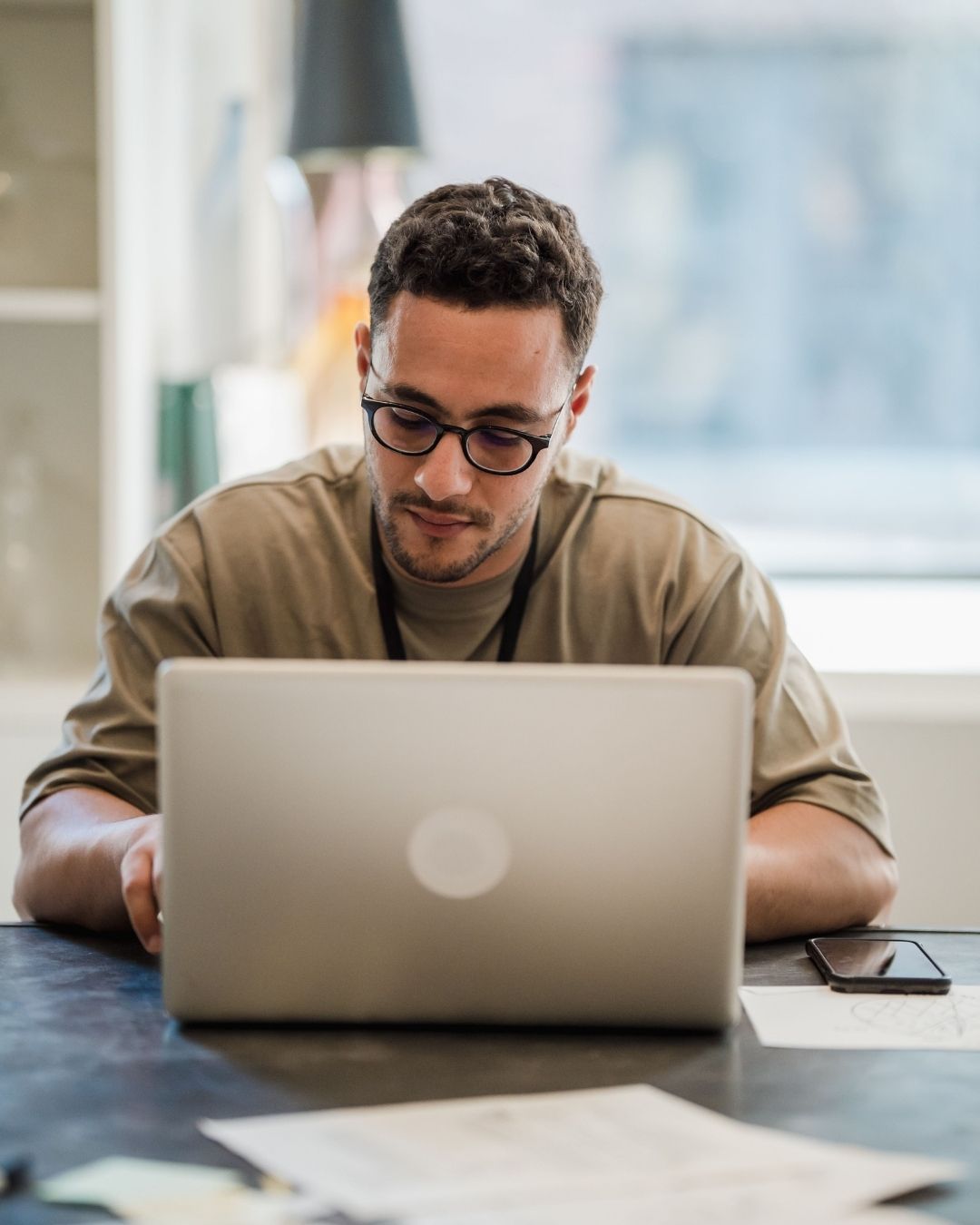A man with glasses and a brown shirt types on a computer.