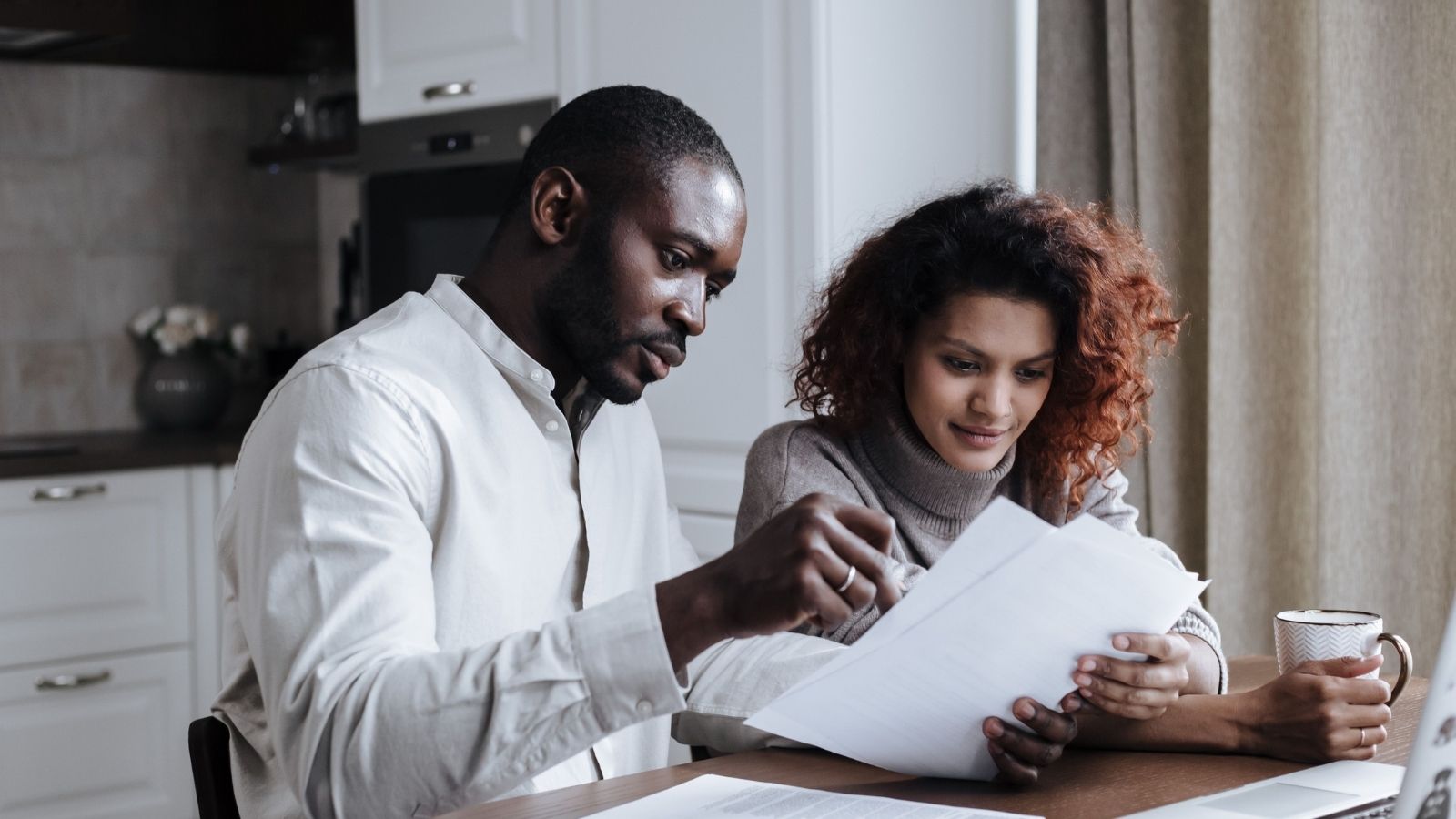 Australian homeowners reviewing renovation quotes, floor plans and budget documents at a kitchen table.