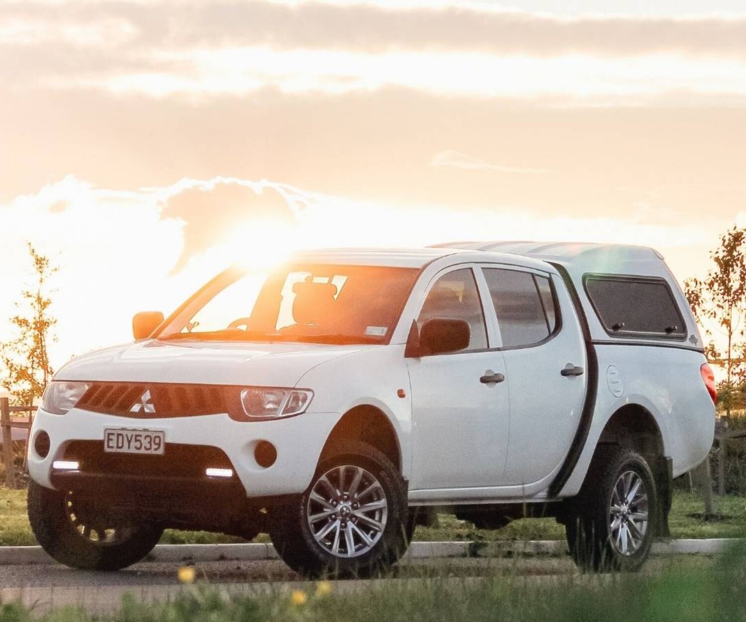 A white ute parked on a road as the sun sets behind it