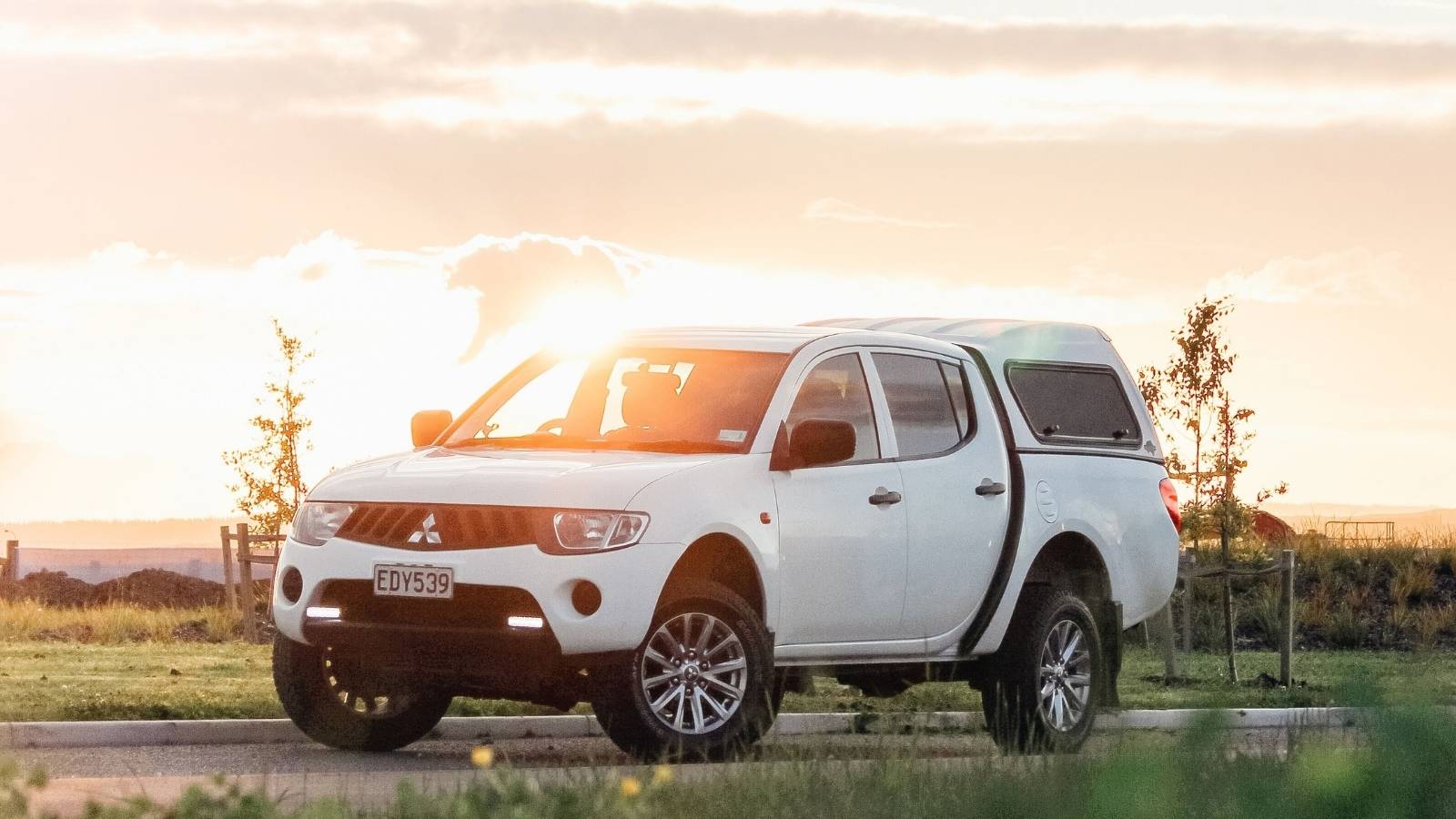 A white ute parked on a road as the sun sets behind it